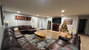 Un salon avec un canapé en cuir marron, une table basse en bois, une cheminée, un téléviseur et un sapin de Noël.