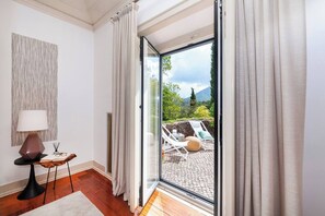 Habitació moderna amb una gran porta corredissa de vidre que dona a una zona exterior amb seients de relaxació i vistes a la vegetació i a les muntanyes.