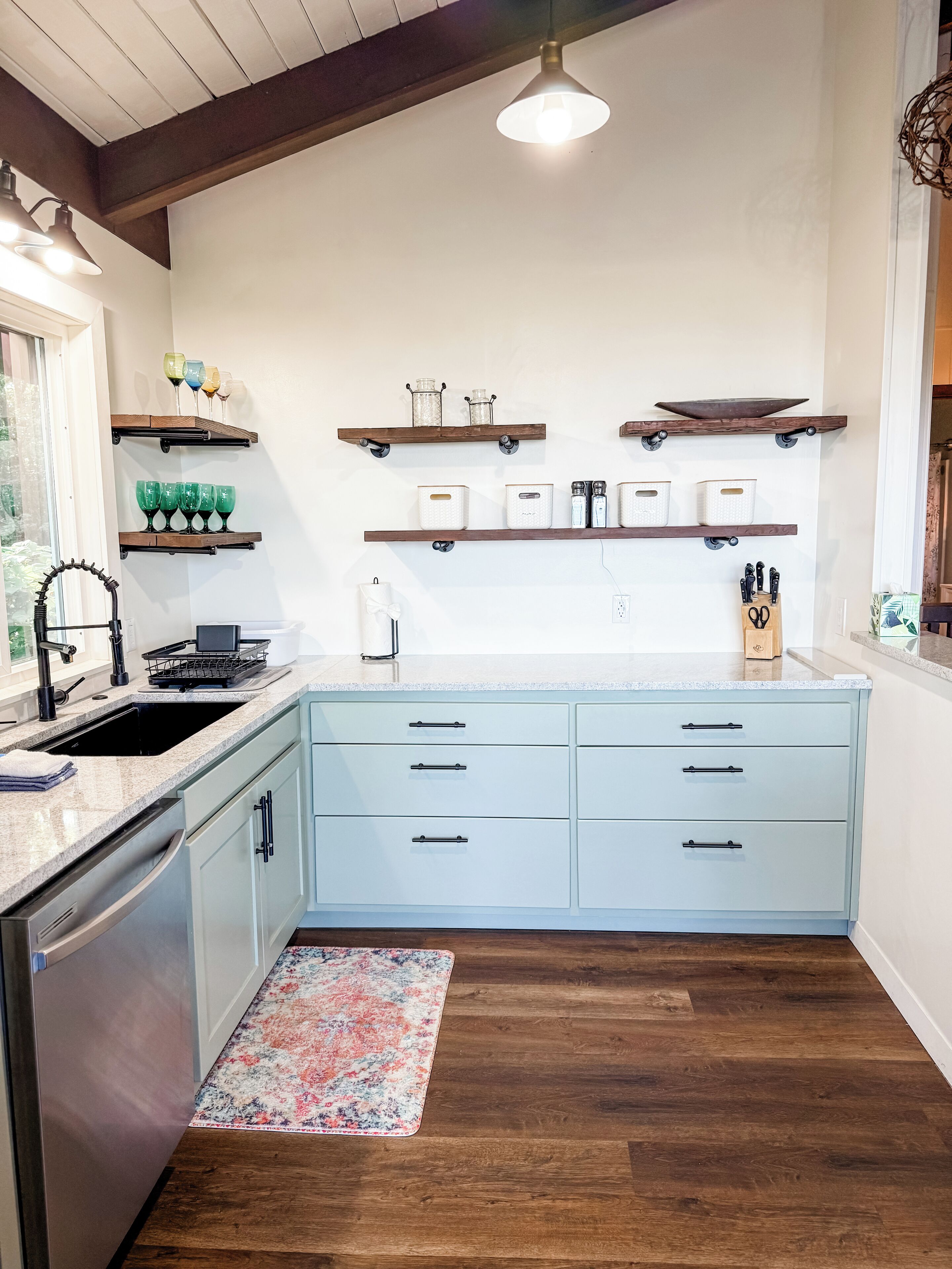 Een keuken met lichtblauwe kastjes, houten planken en een vloerkleed met een patroon.
