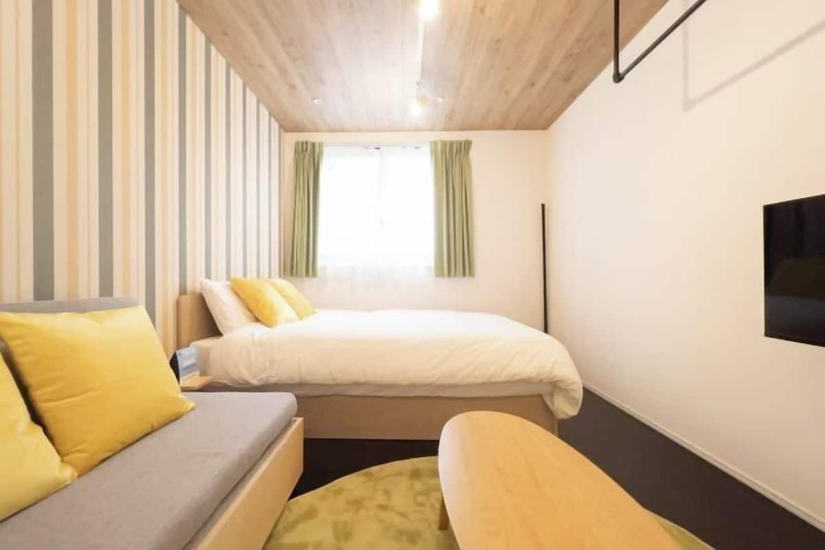 Hotellihuone, jossa on sänky, sohva ja seinälle asennettu televisio.