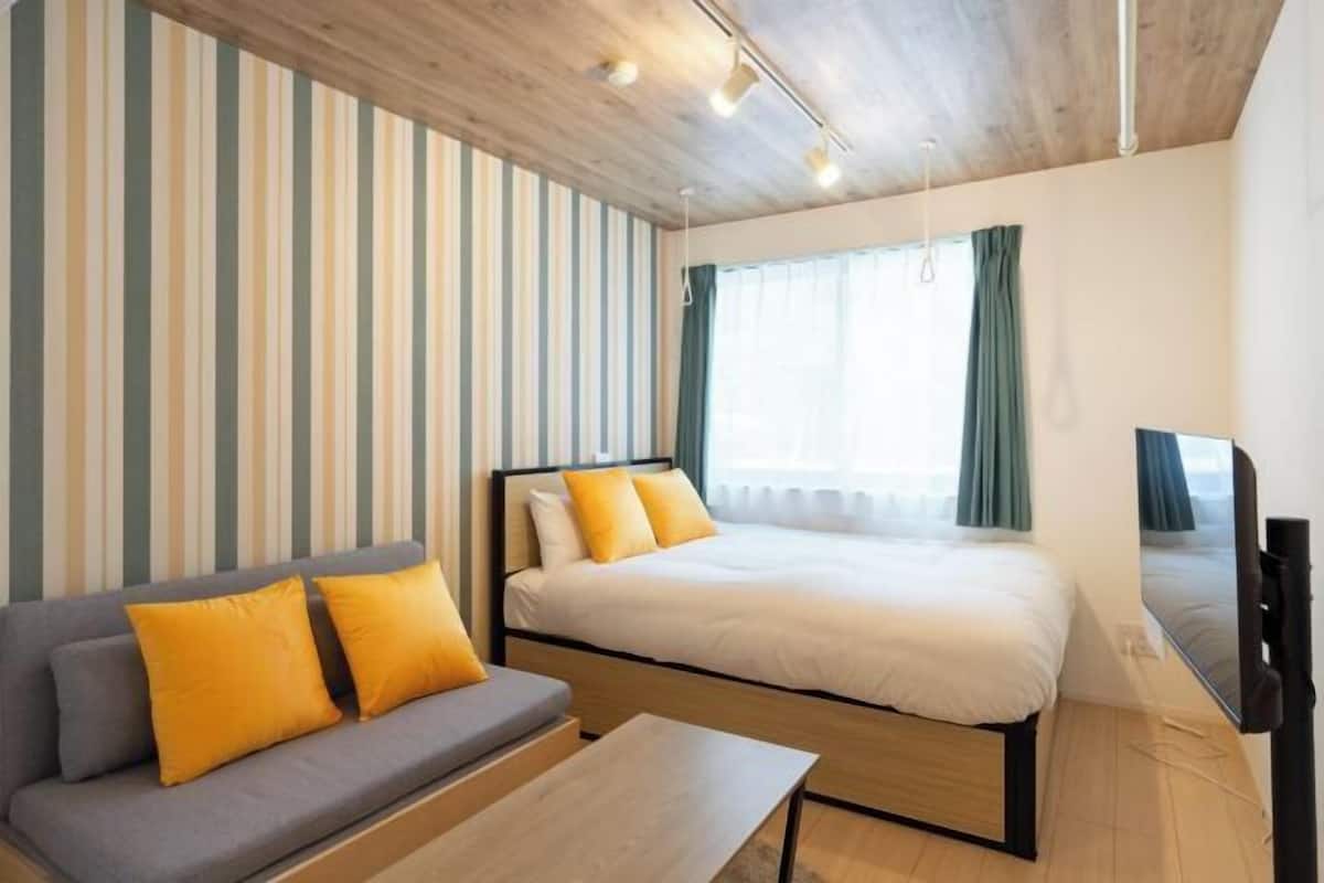 Hotellihuone, jossa on sänky, sohva, televisio ja ikkuna, jossa on verhot.
