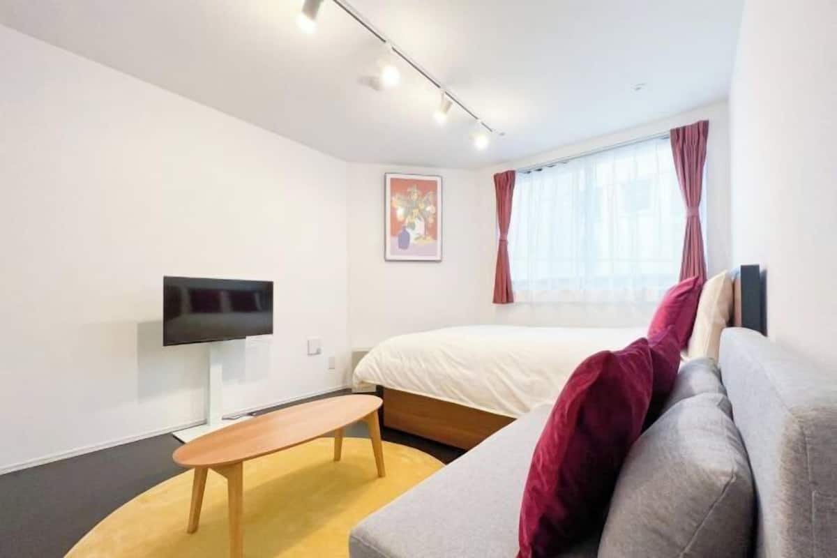 Moderni hotellihuone, jossa on sänky, taulutelevisio, sohva ja pieni pöytä.