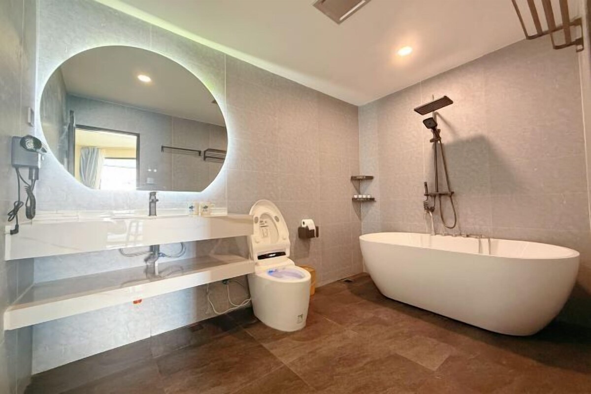 A modern bathroom with a freestanding toilet, a large bathtub, and a wall-mounted shower.