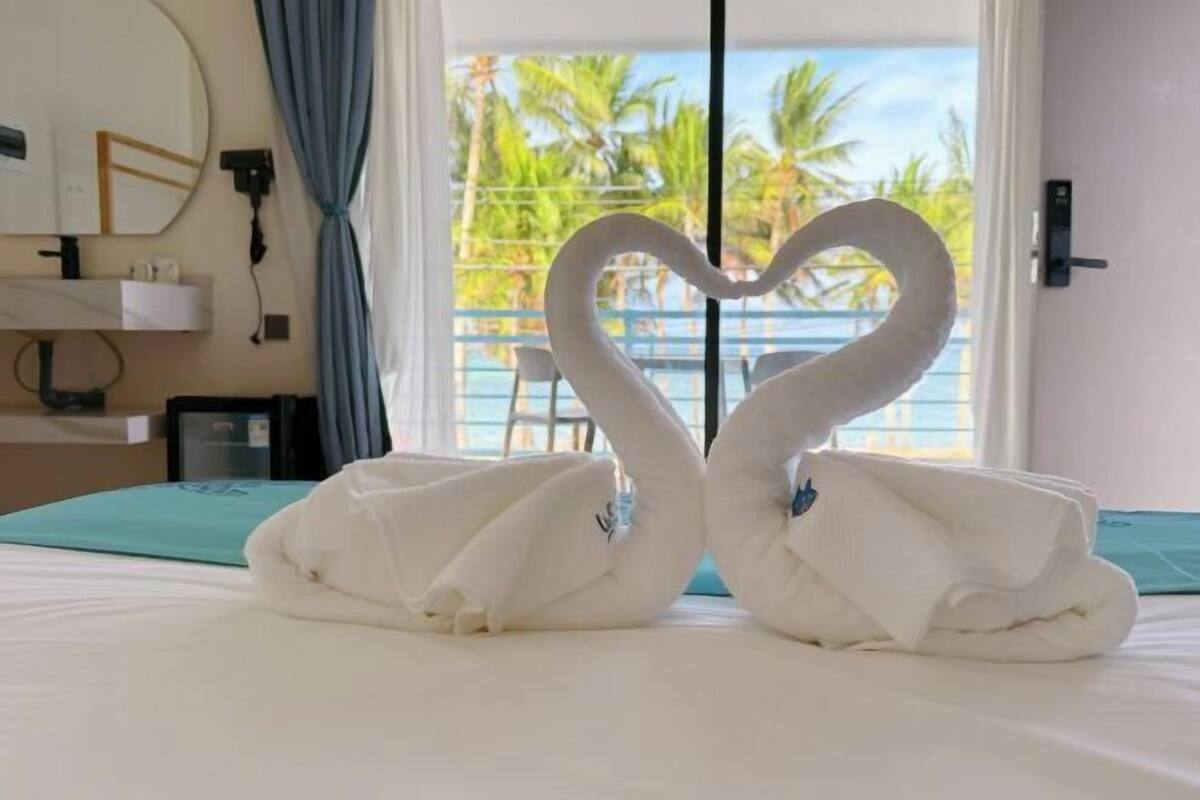 Ein Hotelzimmer mit Bett, Spiegel, Handtuchhalter und Blick auf Palmen durch das Fenster.