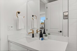 A modern bathroom with a white vanity, gold faucets, and a large mirror.