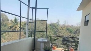 A covered balcony with a table, potted plants, and a blue stool. - Blumint 307 Yelahanka & Blumint 308 (Bengaluru)