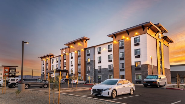 A multi-story hotel with a modern design, featuring a parking lot with several cars.