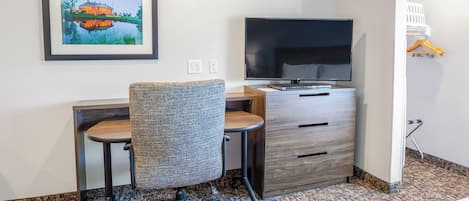 Una habitación de hotel con escritorio, silla, televisión y un cuadro en la pared.
