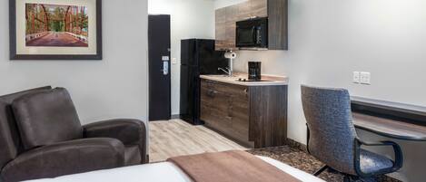 Habitación de hotel con cama, escritorio, silla, kitchenette y un cuadro en la pared.
