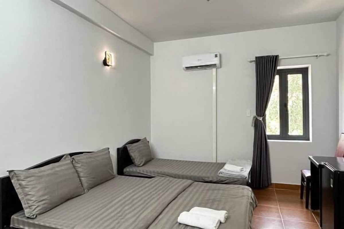 A room with two beds, a desk, an air conditioning unit, and a window with curtains.