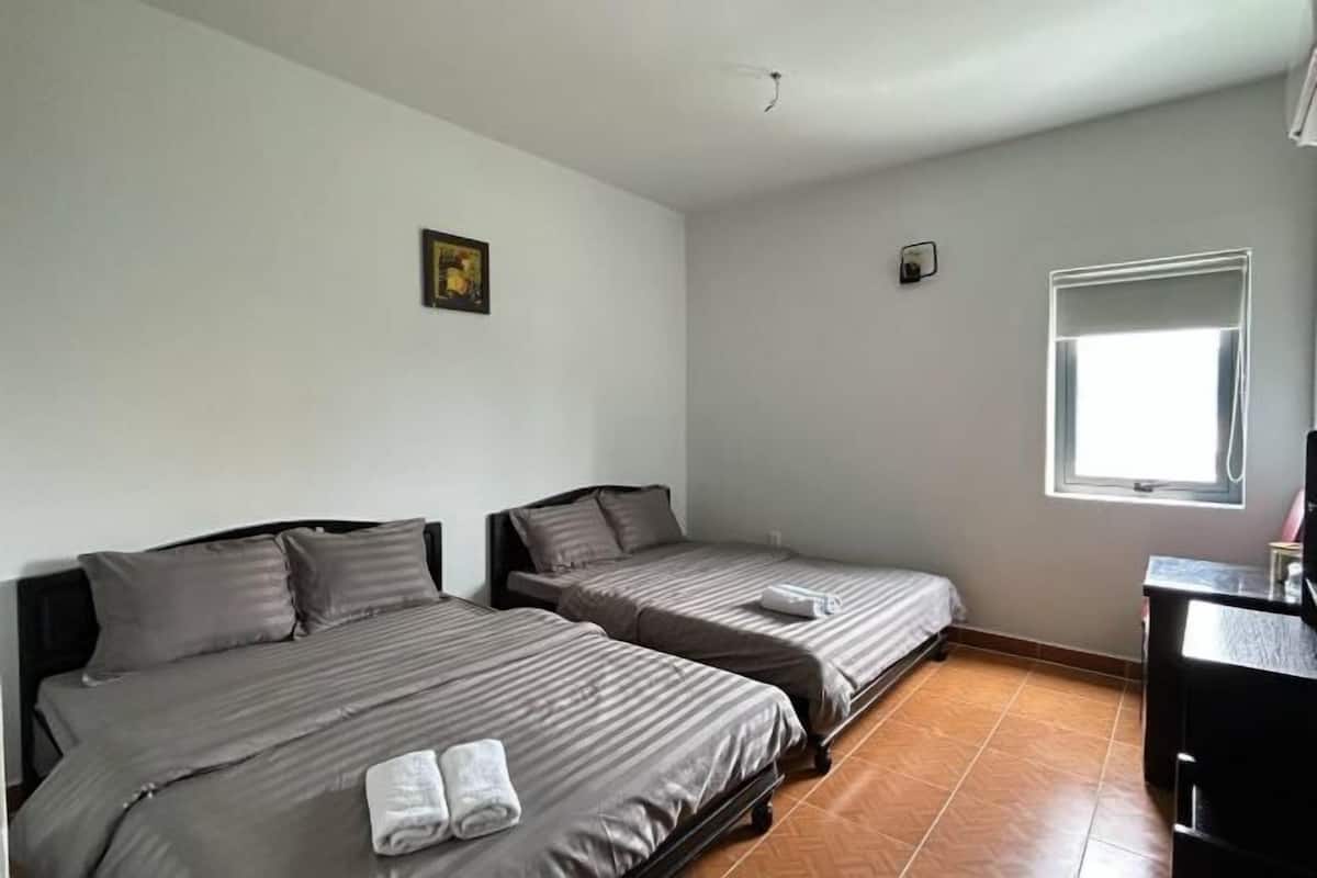 A room with two beds, a small desk, a window, and a painting on the wall.