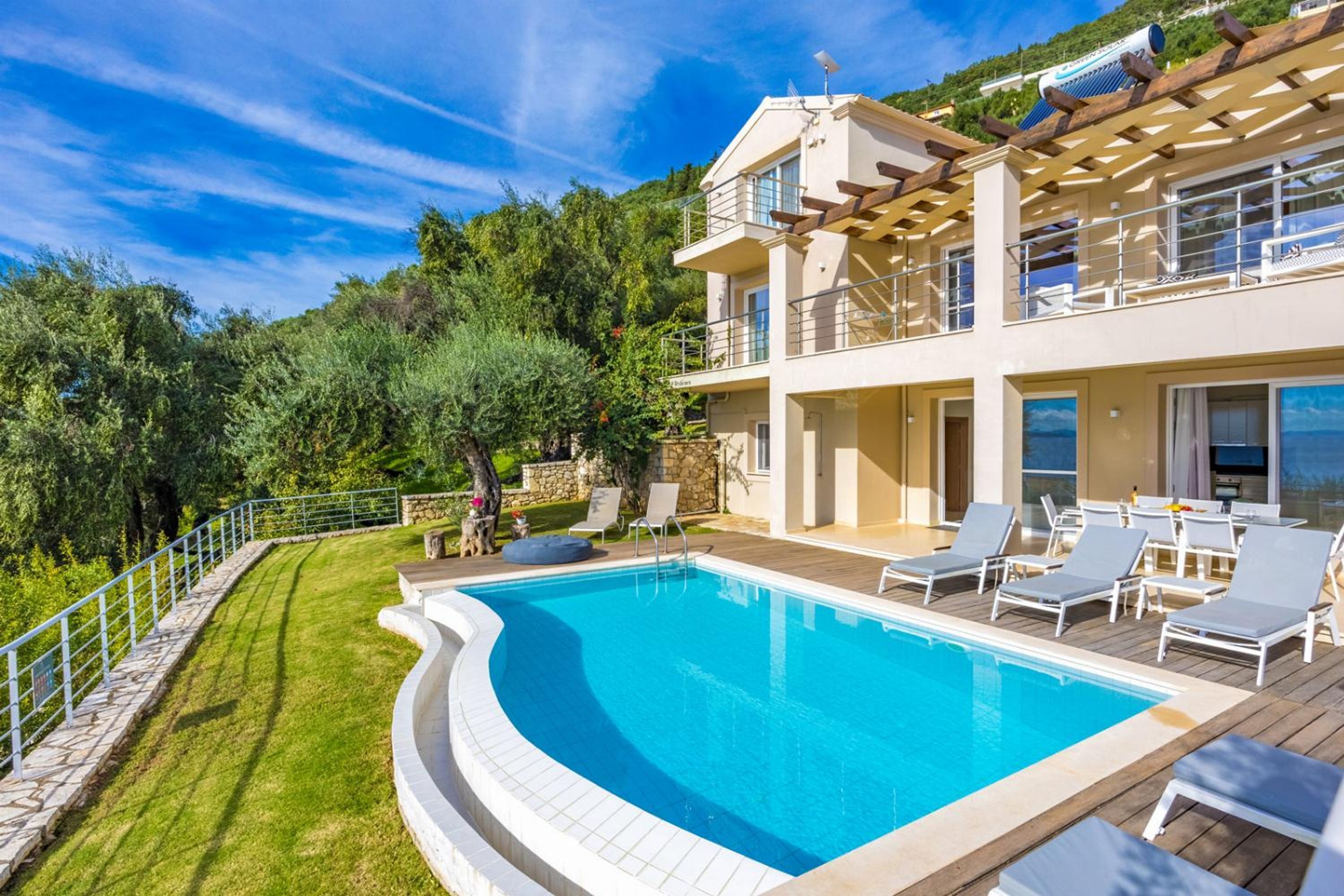 Una casa de dos pisos con piscina, mobiliario exterior y vistas a la vegetación circundante.