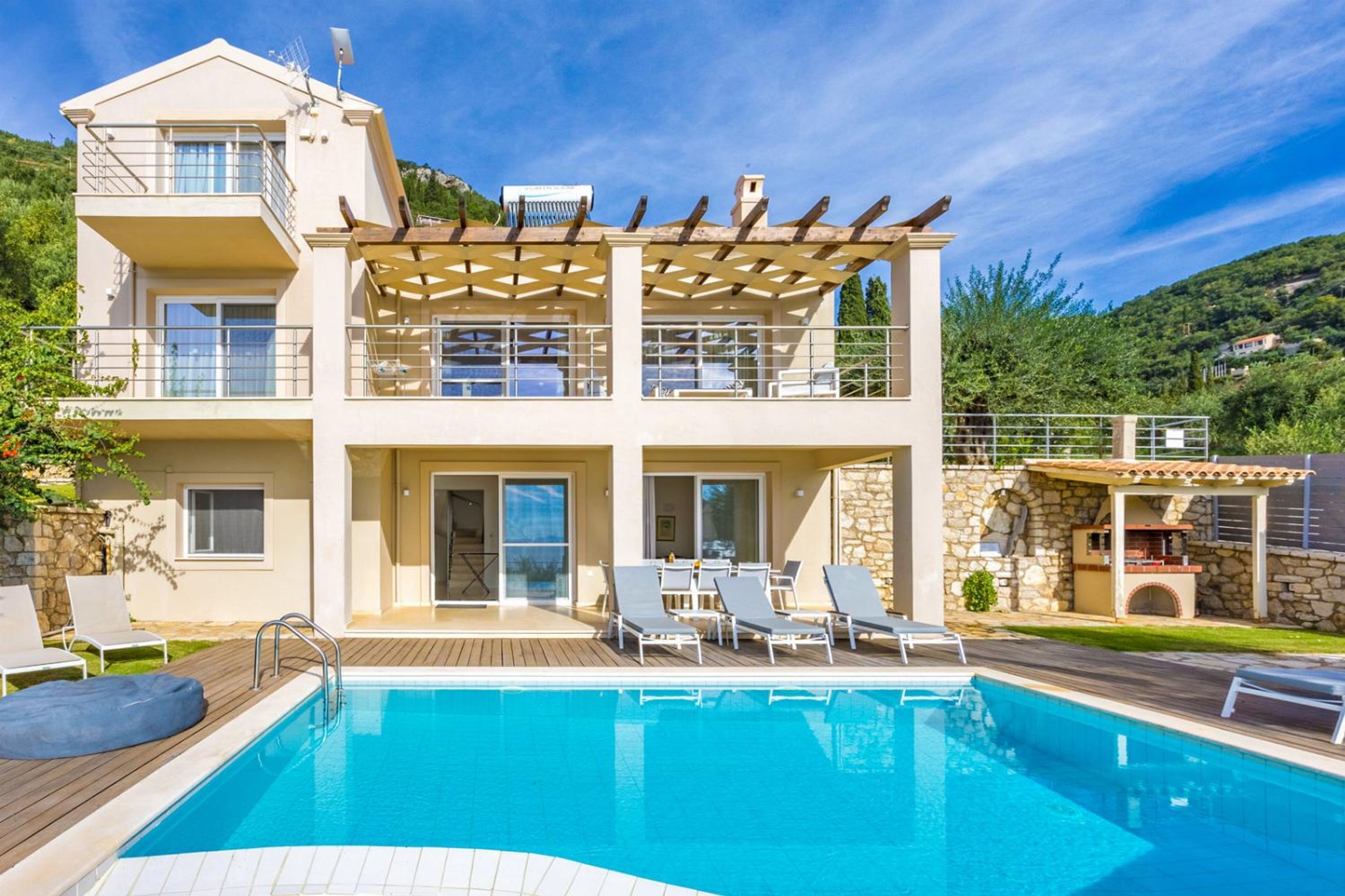 A two-story house with a swimming pool, outdoor seating, and a stone wall.