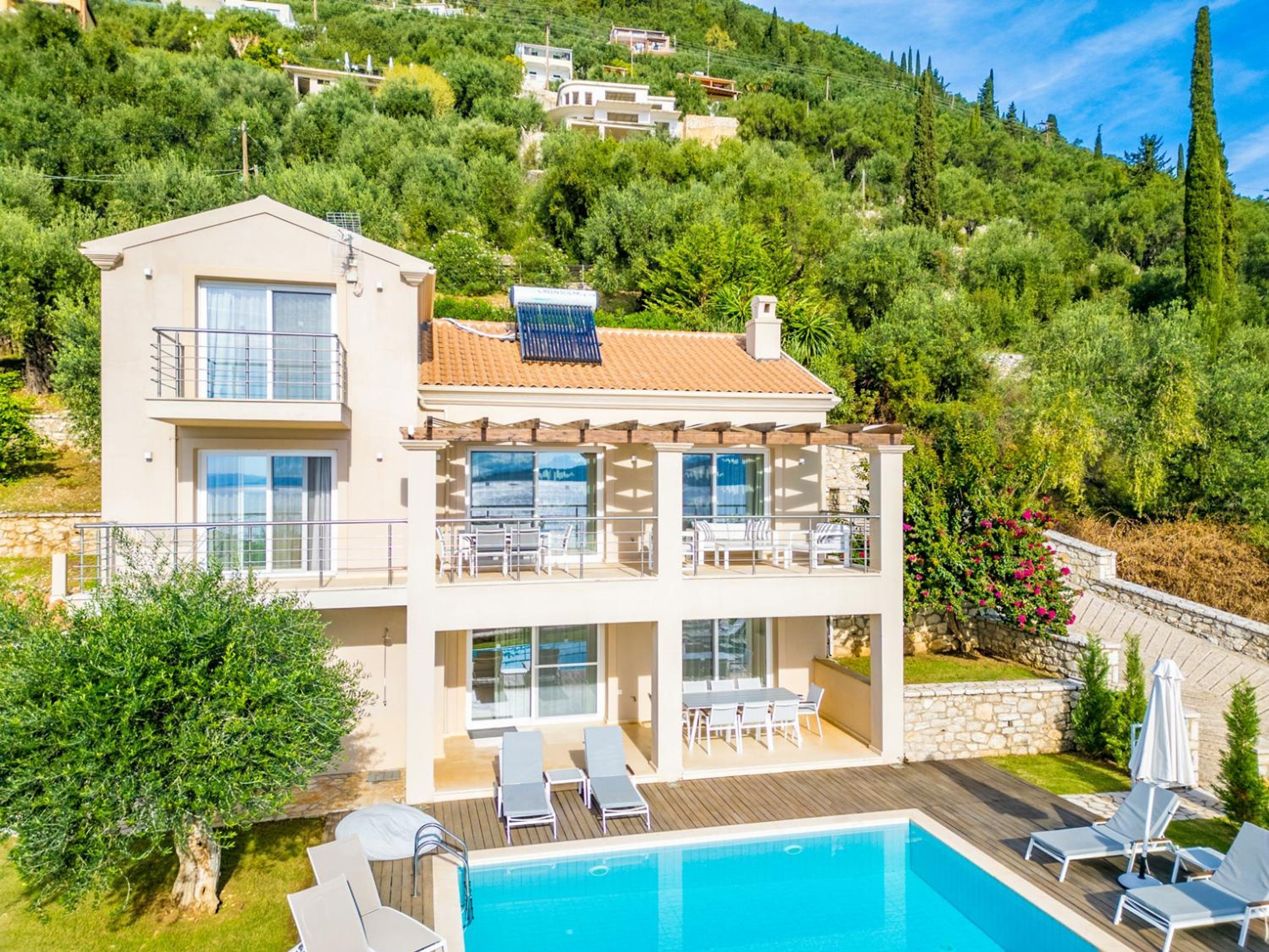 Una casa de dos pisos con piscina, mobiliario exterior y vistas a una colina.