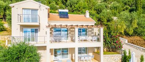 Una casa de dos pisos con piscina, mobiliario exterior y vistas a una colina.