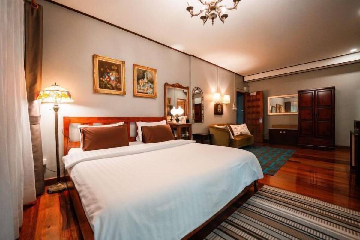A hotel room with a large bed, a desk, a chair, a wardrobe, and a chandelier.