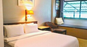 A hotel room with a bed, a nightstand, a chair, a window, and a wall-mounted lamp. - Ban Mai Vintage (Pak Chong)