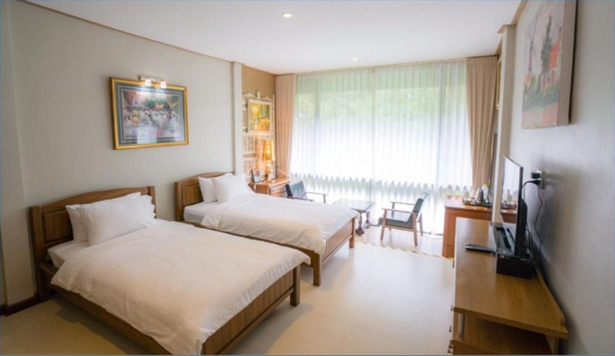 Een hotelkamer met twee bedden, een bureau, een stoel, een televisie en een raam met gordijnen.