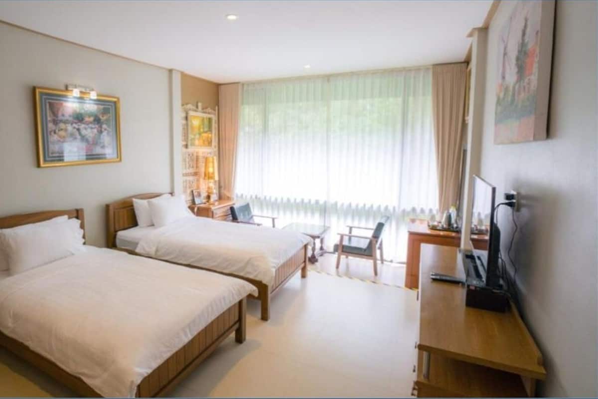 A hotel room with two beds, a desk, a chair, a TV, and a window with curtains.