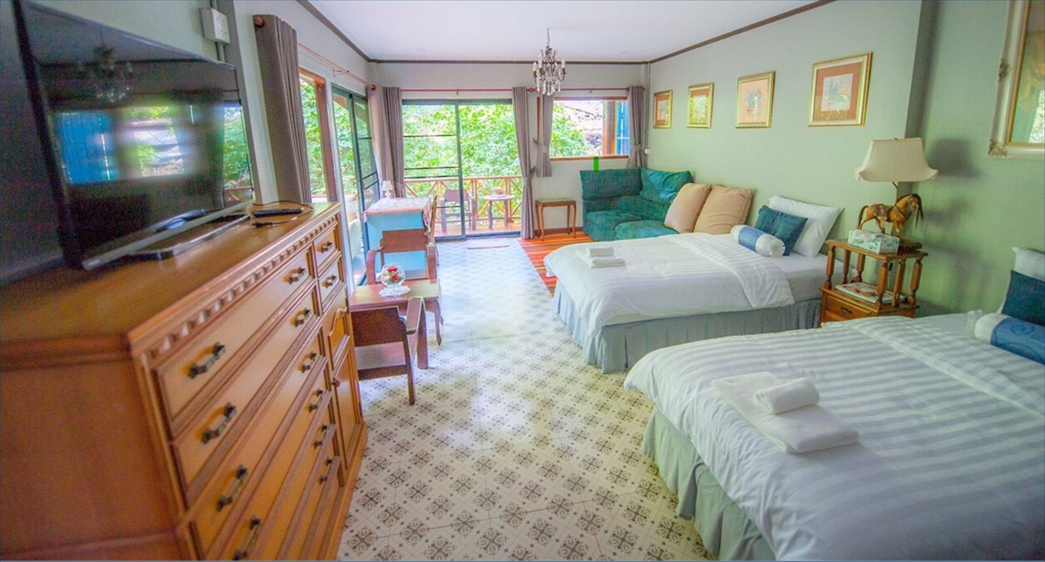 A hotel room with two beds, a television, a dresser, a chair, and a balcony with a view of greenery.