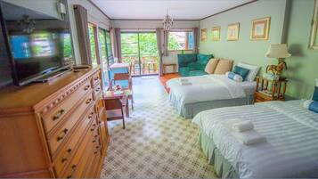 A hotel room with two beds, a television, a dresser, a chair, and a balcony with a view of greenery.