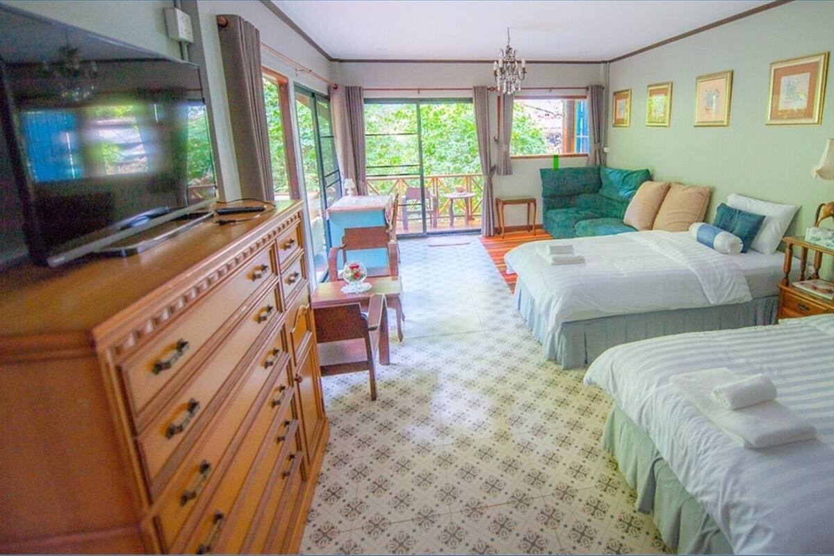 A hotel room with two beds, a television, a dresser, a chair, and a balcony with a view of greenery.
