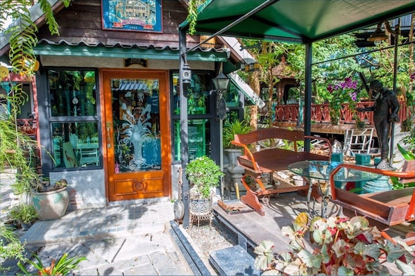 A traditional wooden building with a green awning, a glass door, and a small porch area with a bench and potted plants. - Ban Mai Vintage (Pak Chong)