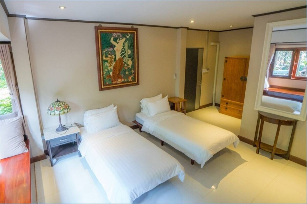 A room with two beds, a nightstand, a lamp, a painting, a mirror, and a window.