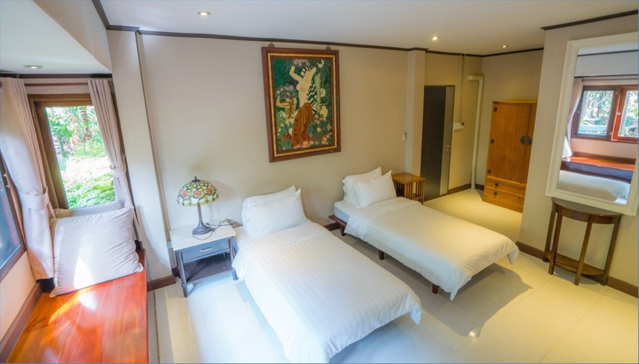 Une chambre avec deux lits, une table de chevet, une lampe, un tableau, un miroir et une fenêtre.