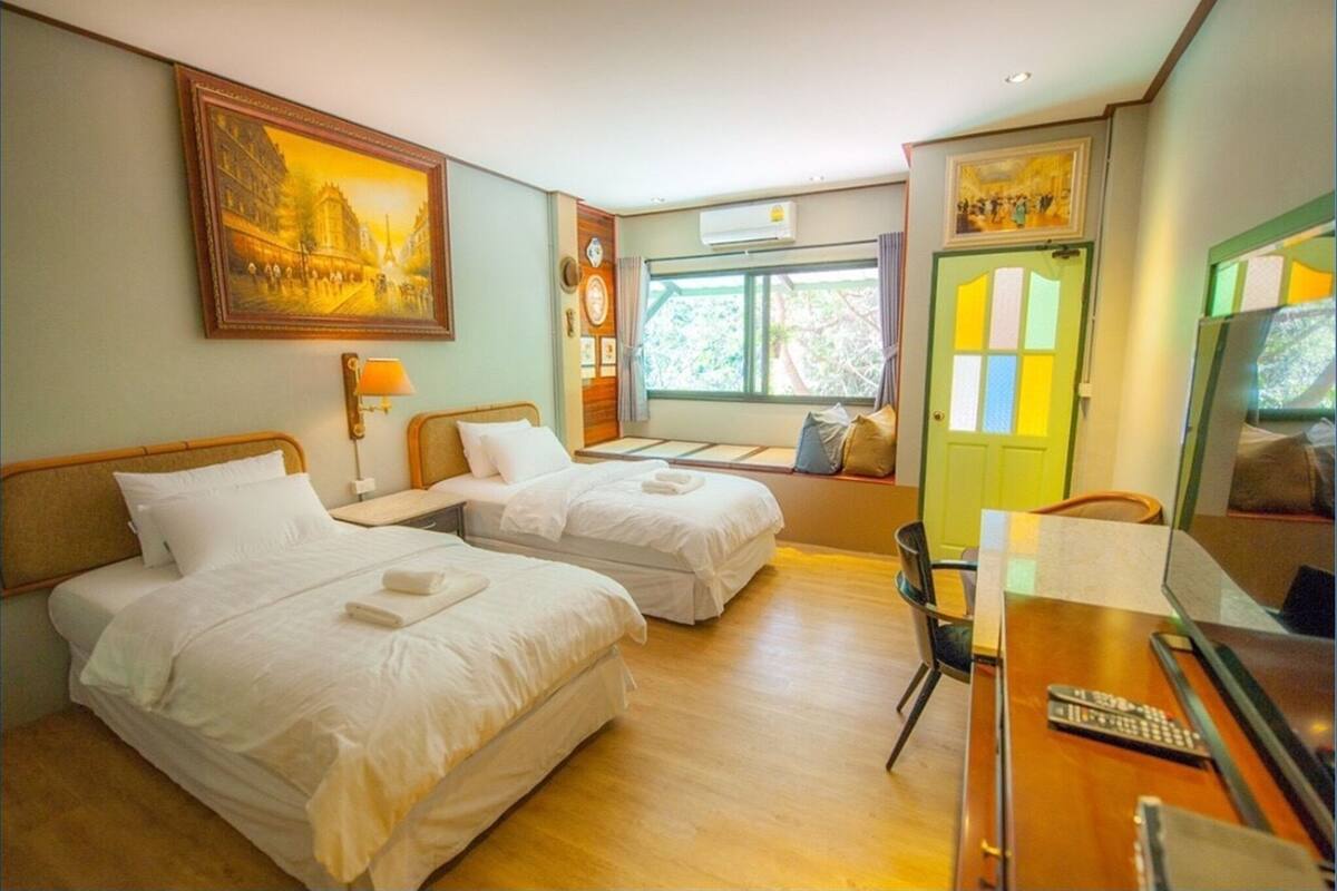 A hotel room with two beds, a desk with a chair, a television, and a window with curtains.