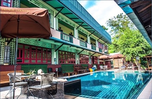 A poolside area with outdoor seating and a two-story building with traditional architectural elements. - Ban Mai Vintage (Pak Chong)