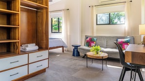 A modern room with a wooden wardrobe, a grey sofa, a small round table with a plant, and a bed with a white duvet. - Casa Amor, 1-bedroom Villa with salt water pool, garden & mountain views (Ojochal)
