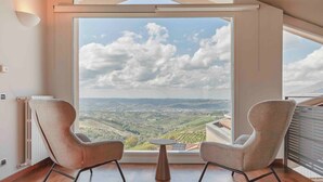 A room with a large window offering a view of a valley. There are two chairs and a small table in the room. - The Vista Retreat N.1 (Treiso)