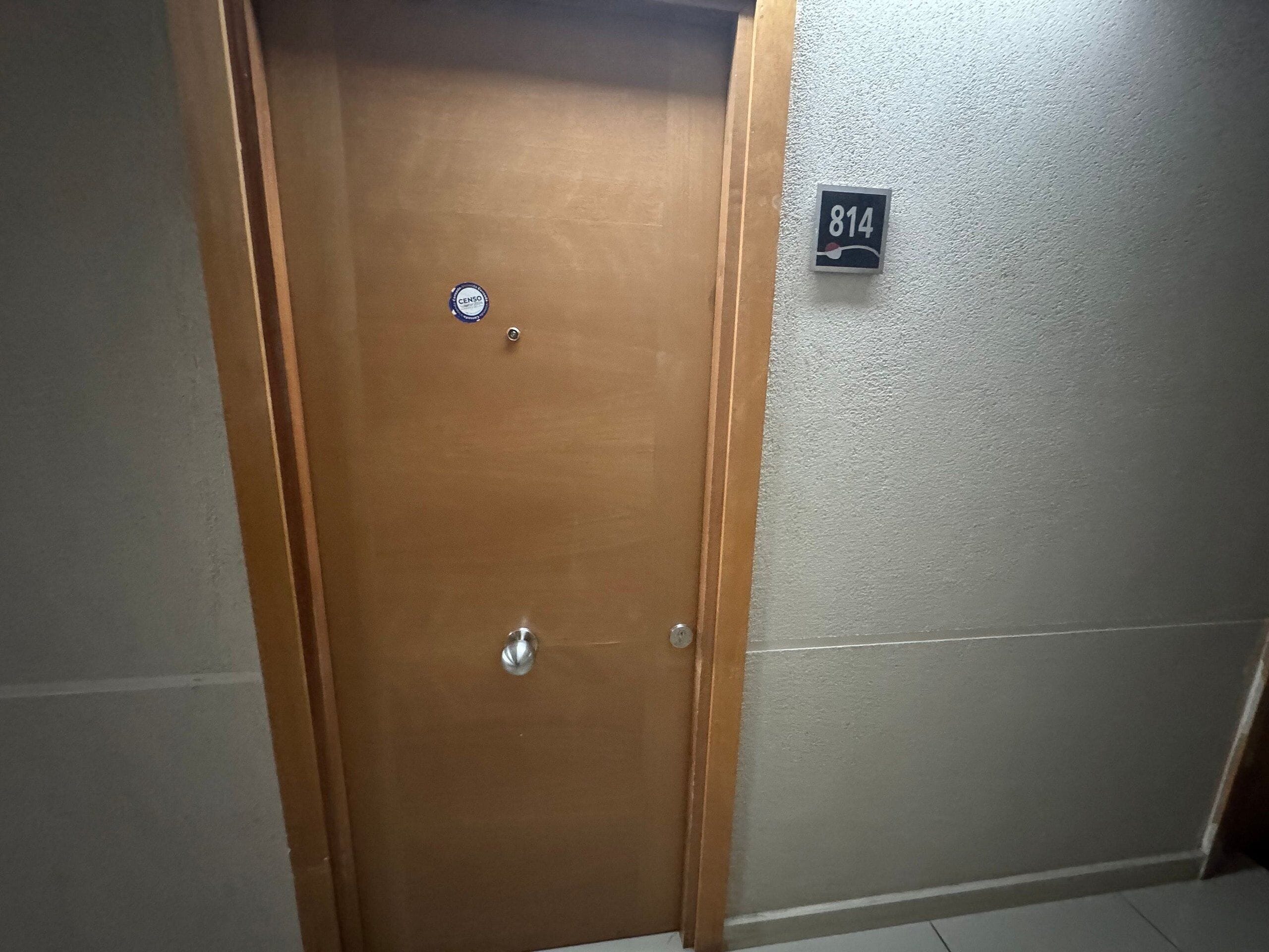 Uma porta de madeira com um adesivo CENSO, um interfone e uma placa com o número 814.