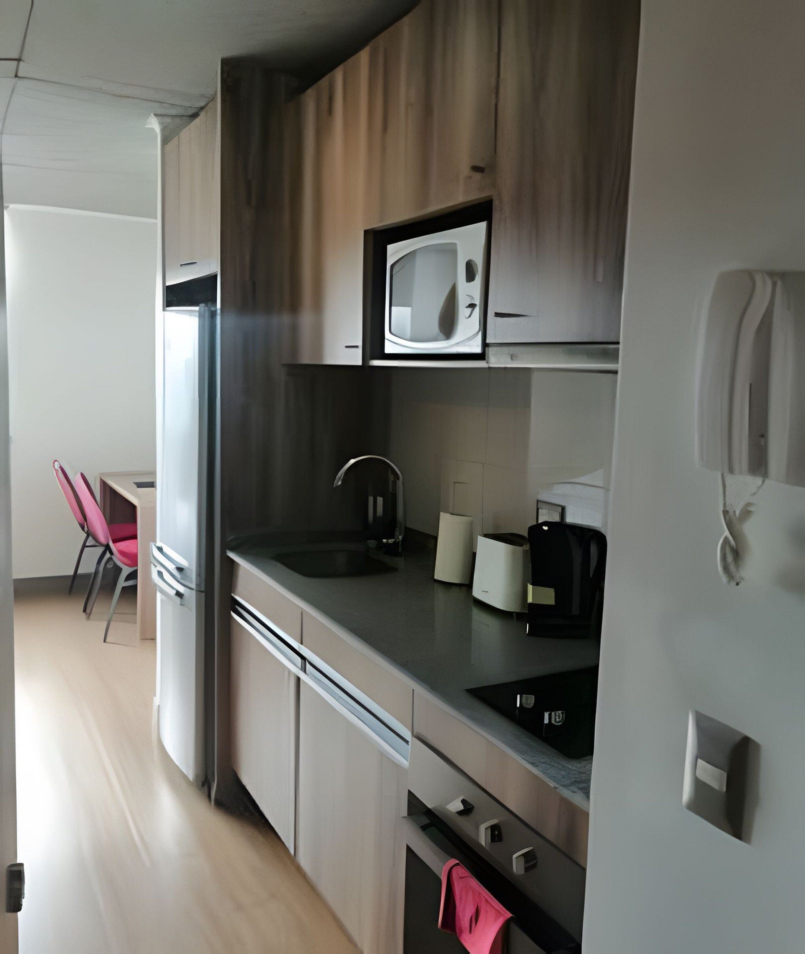 A modern kitchen with a microwave, sink, and stove. There is a chair and a table in the adjacent room.