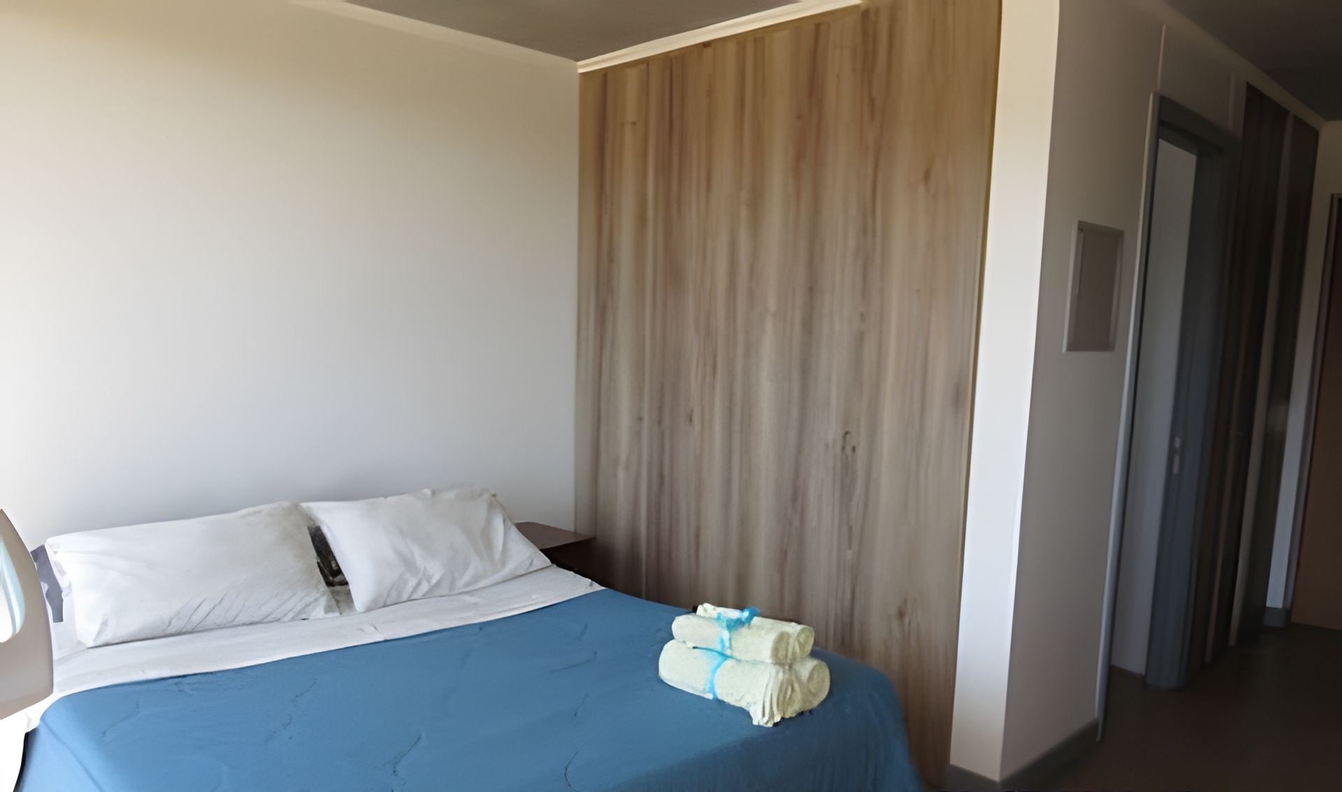 A bedroom with a bed, a wooden panel wall, and a hallway.