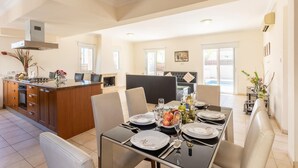A spacious dining area with a central island, a kitchen with a stove, and a seating area with a sofa. - Villa Solis With 3 Bedrooms and 3 Bathrooms (Paralimni)