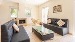 A modern living room with a fireplace, two sofas, a glass coffee table, and a painting on the wall. - Villa Solis With 3 Bedrooms and 3 Bathrooms (Paralimni)