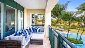 A balcony with a sofa, a view of a pool, and palm trees.