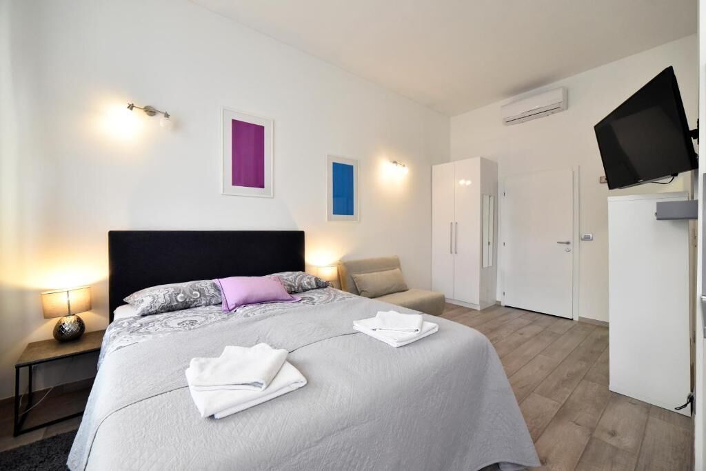 A hotel room with a bed, bedside lamp, wardrobe, and a television.