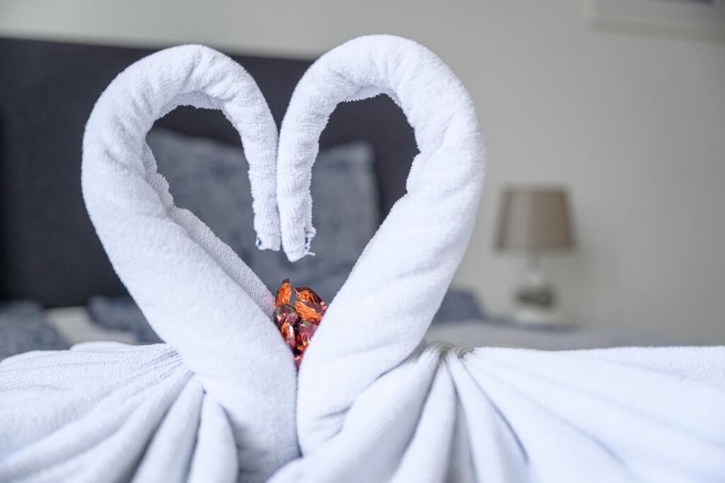 A bed with white towels arranged in a heart shape.