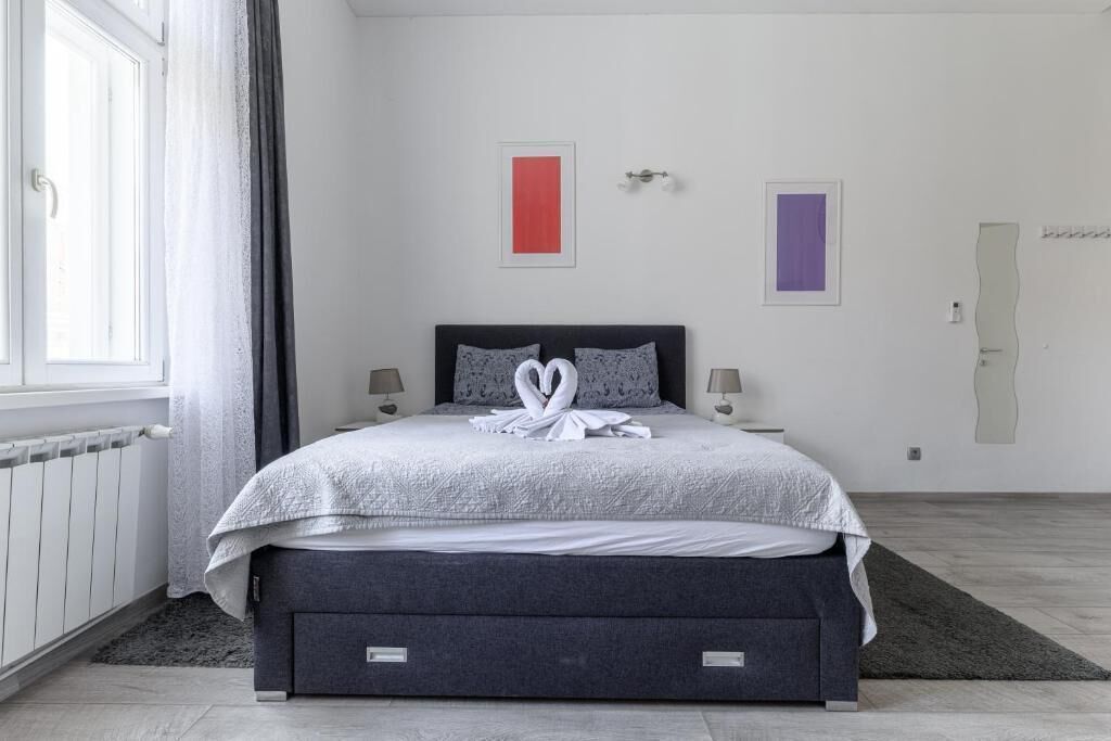 A modern bedroom with a bed, two bedside tables, a radiator, and a window with curtains.