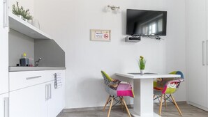 A modern kitchen with a flat-screen TV mounted above the counter, a small table with chairs, and a sign indicating free Wi-Fi. - Deluxe Apartments Ria (Zagreb)