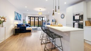 A modern kitchen with a central island, bar stools, and a dining area with a blue sofa and a small table.
