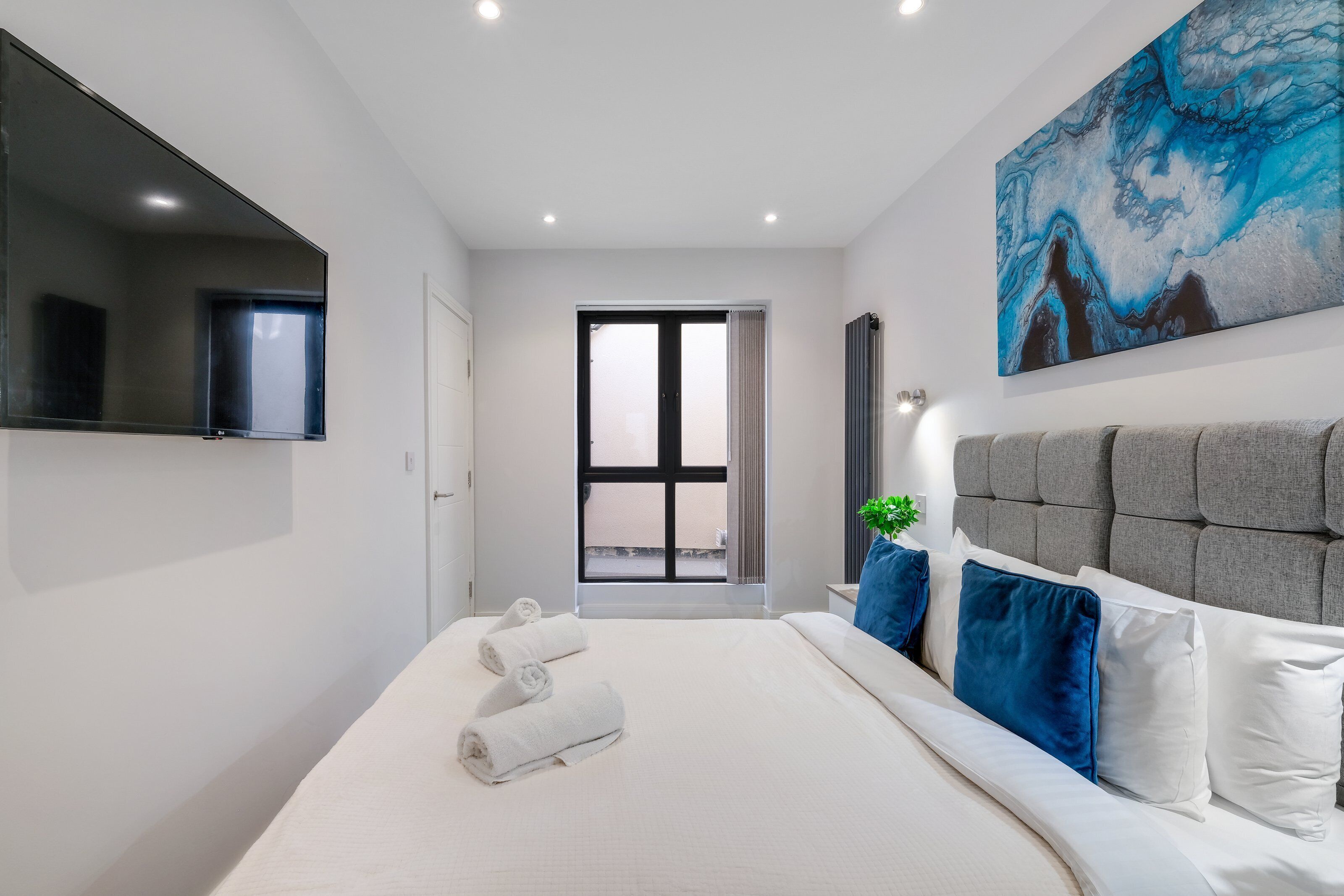 Ein modernes Hotelzimmer mit einem großen Bett, einem Flachbildfernseher, einem Gemälde und Blick durch eine Glastür.