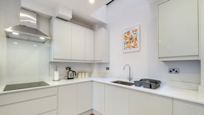 A modern kitchen with white cabinetry, a stainless steel range hood, a sink, and a countertop with a kettle and containers.