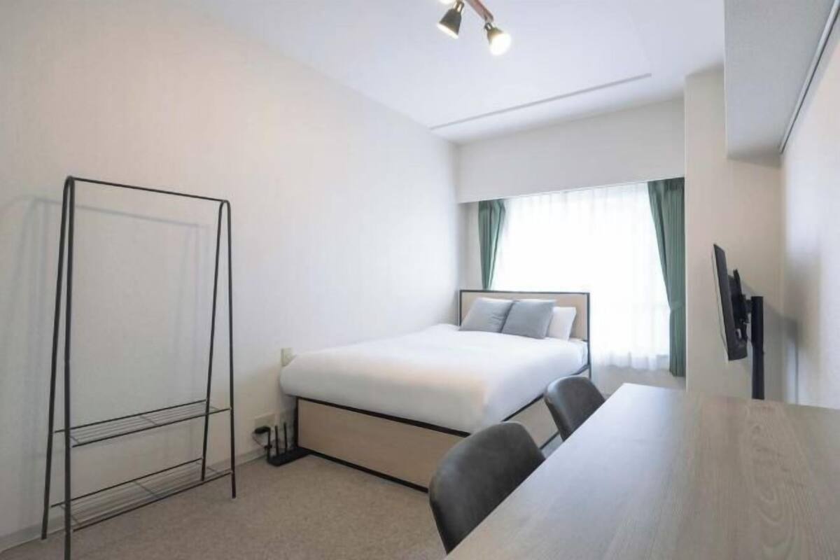 Une chambre d’hôtel avec un lit, un bureau, une chaise, une télévision et une fenêtre avec des rideaux.