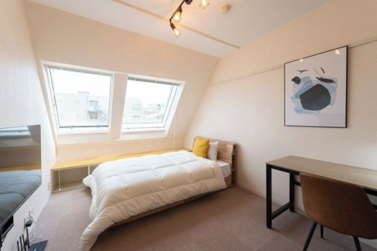 Una camera da letto con un letto, una scrivania, una sedia, una finestra e un'opera d'arte appesa al muro.
