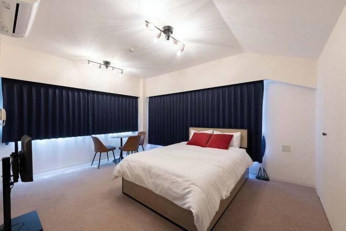 Une chambre d’hôtel moderne avec un grand lit, deux fauteuils, un bureau et un ventilateur de plafond.