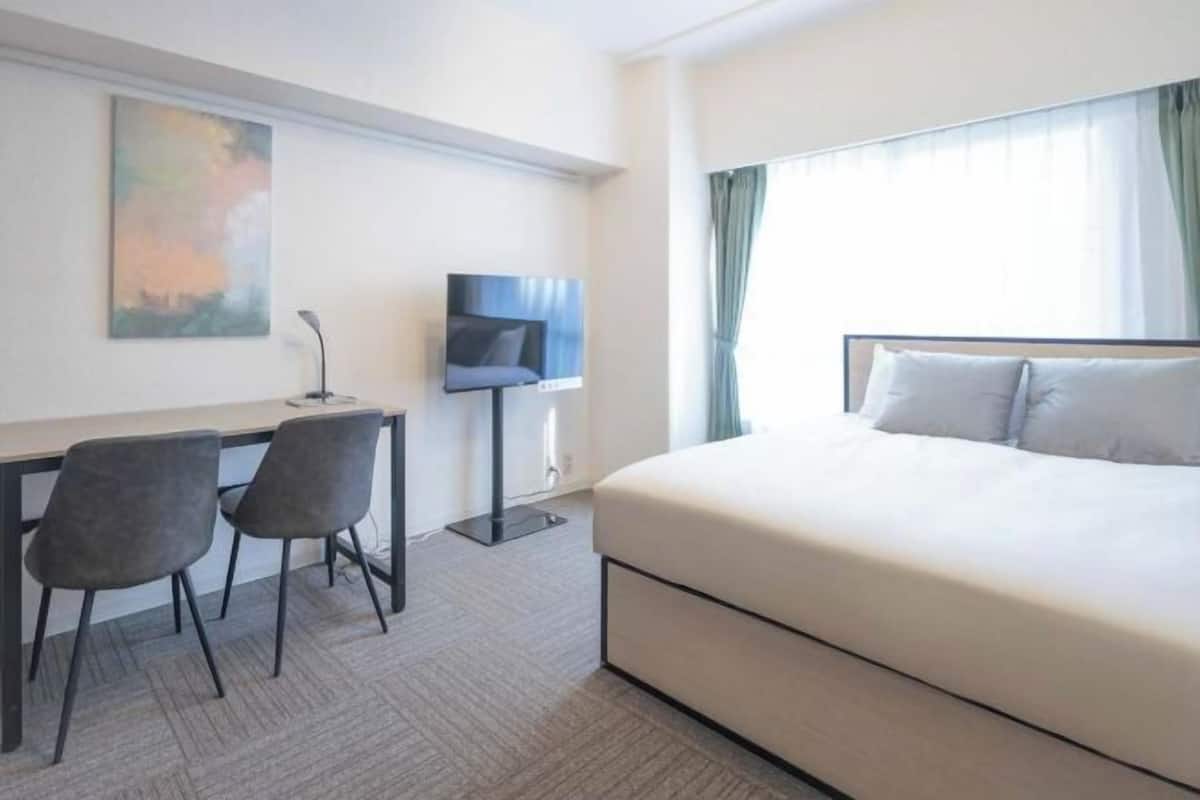Une chambre d’hôtel avec un lit, un bureau avec deux chaises, une télévision et un tableau au mur.
